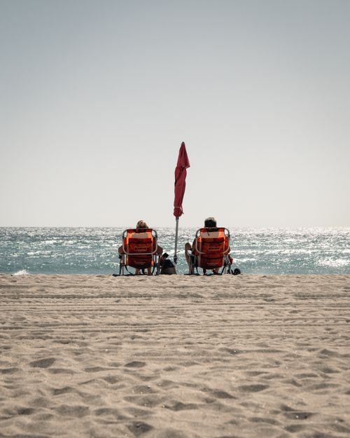 Free Two adults relaxing on a sandy beach with beach chairs and umbrella in Hollywood, Florida. Stock Photo