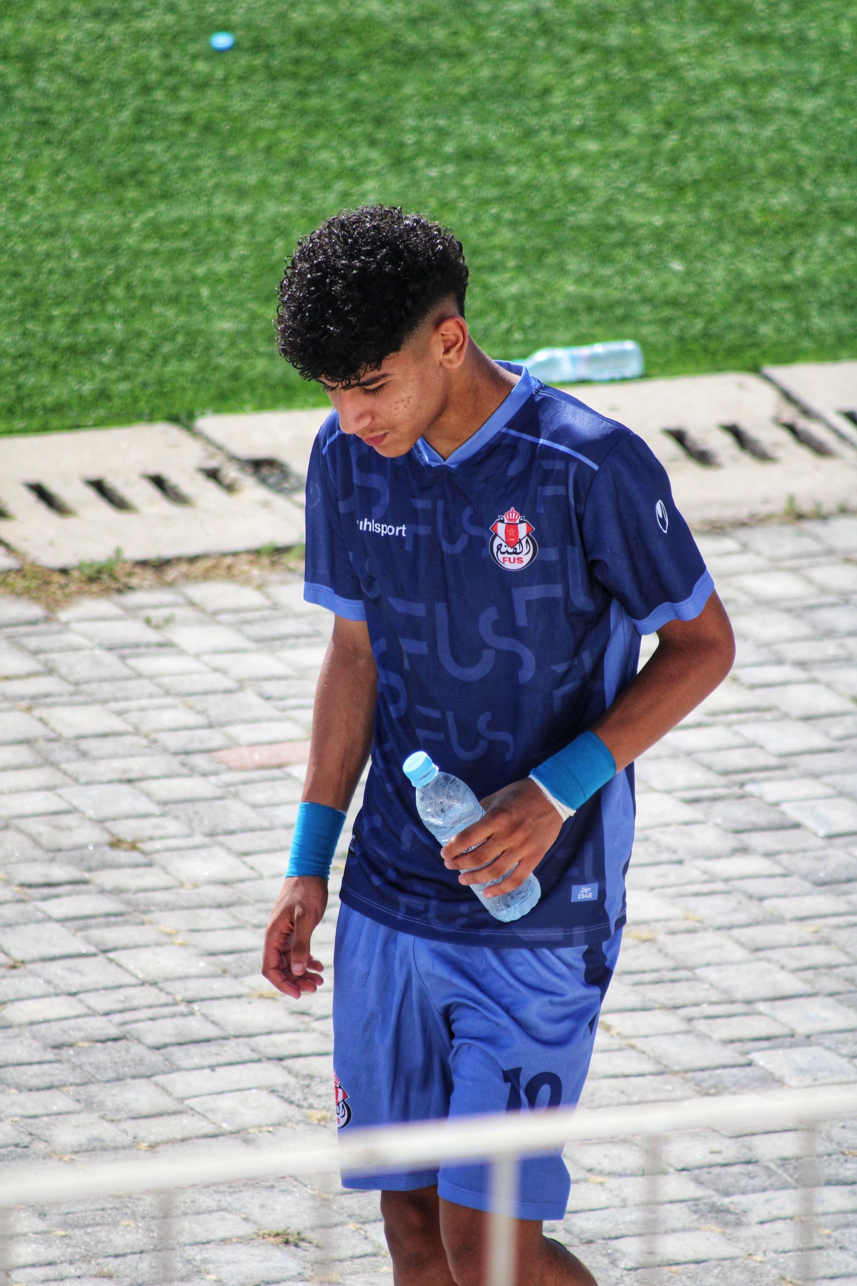 Teen soccer player walking on sports field holding water bottle in Rabat, Morocco.