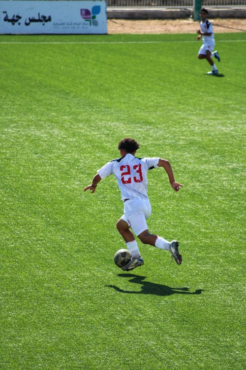 Free Teen soccer player wearing number 23 dribbles on a sunny outdoor field. Stock Photo
