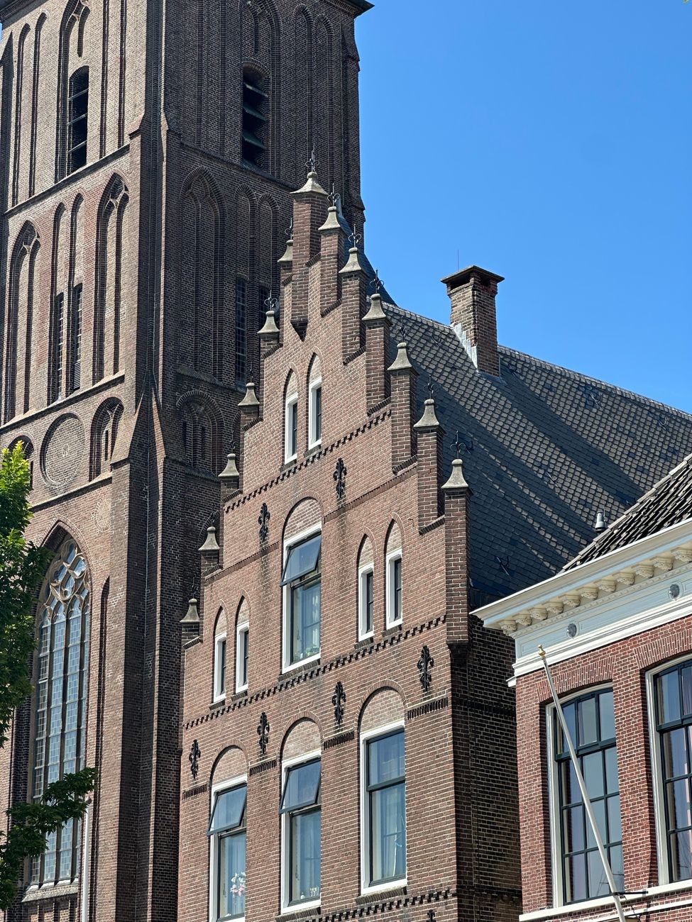 Foto van een historisch Nederlands bakstenen gebouw met gotische elementen op een zonnige dag.