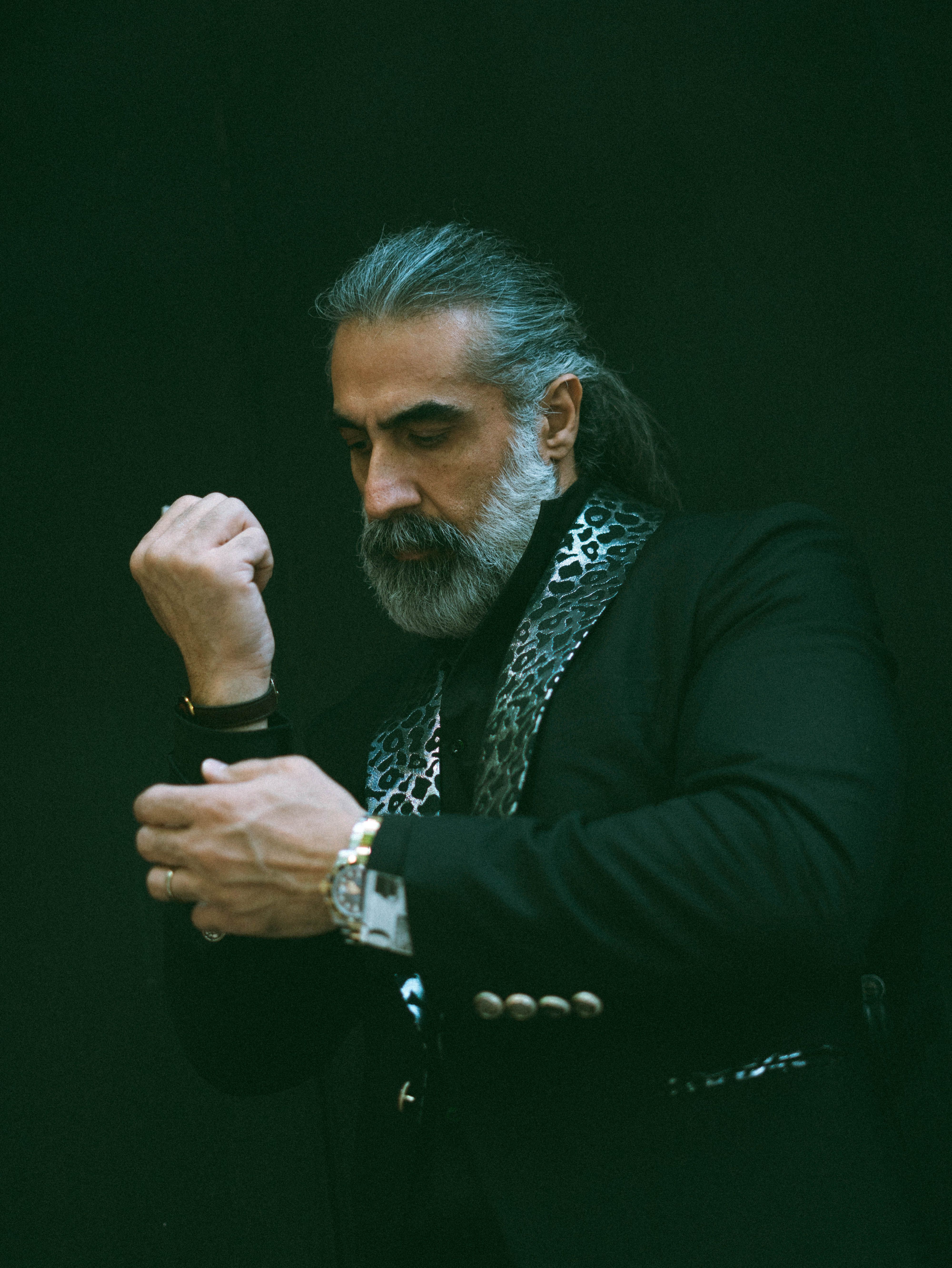 Elegant mature man with gray hair and beard adjusting his formal suit, exuding style.