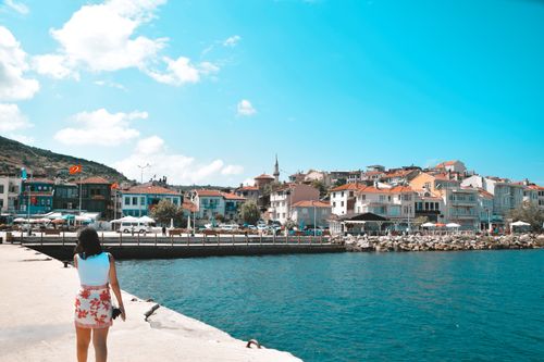Free A woman walks along a waterfront in a vibrant Turkish coastal town under a clear blue sky. Stock Photo