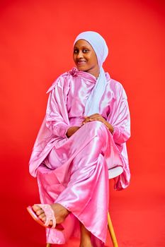 Stylish woman in a pink silk outfit poses against a vibrant red backdrop.
