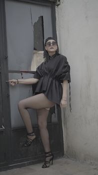 Woman in stylish black outfit poses against a distressed door in an urban setting.
