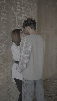 A romantic couple shares an intimate moment inside a rustic brick-walled room, conveying warmth and connection.