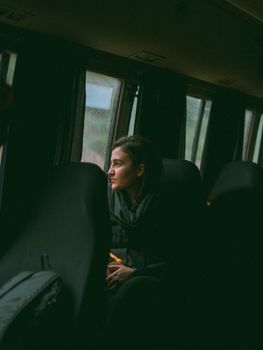 A woman in a bus looking out the window thoughtfully on a rainy day.