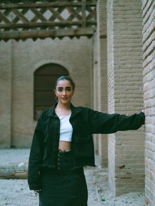 Free Stylish woman in a black jacket and white top poses against a historic brick wall outdoors. Stock Photo