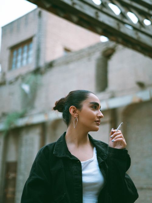 Free Portrait of a woman smoking in a casual urban setting with brick buildings in the background. Stock Photo