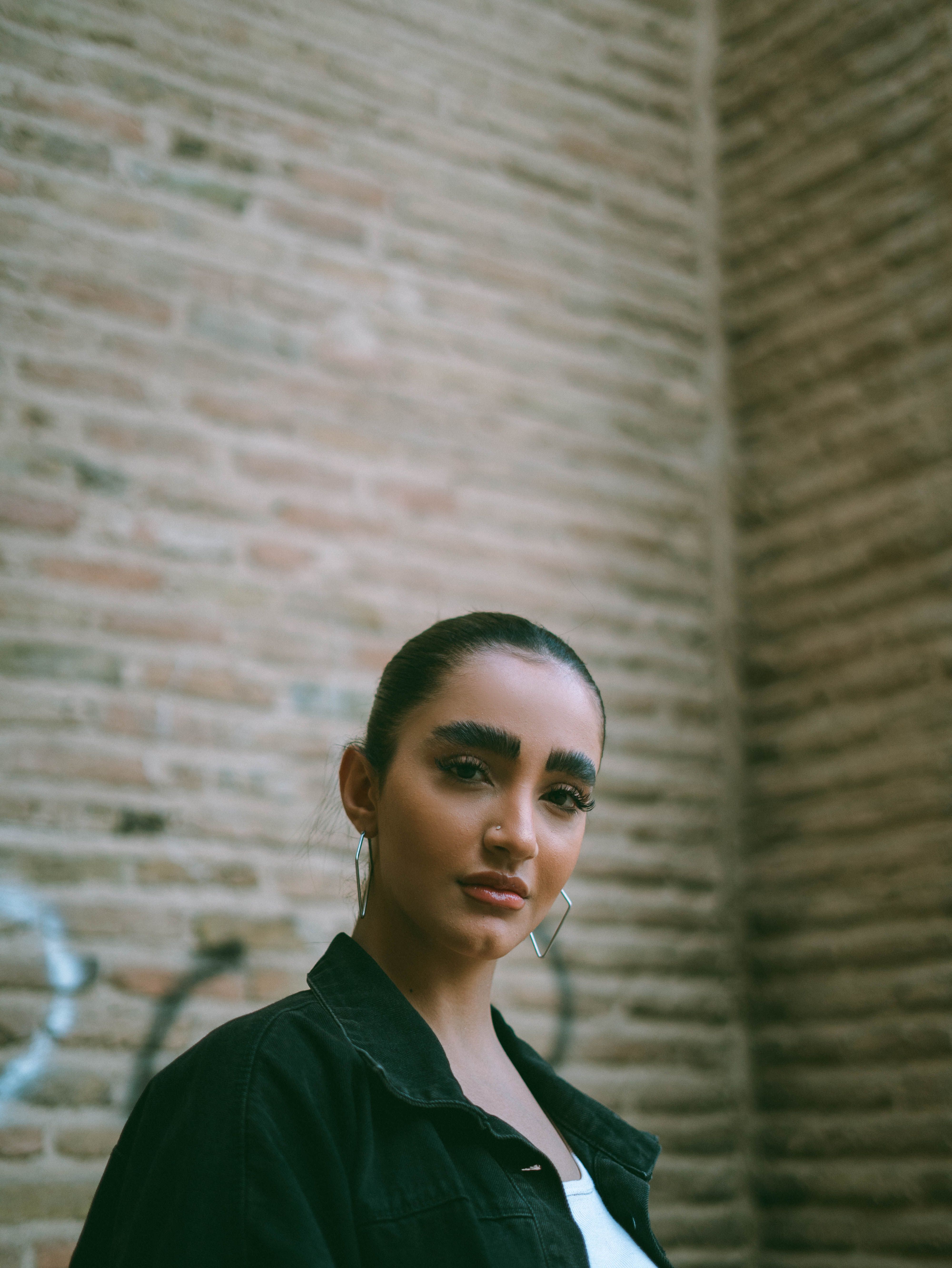 Stylish woman poses confidently against an urban brick wall backdrop.