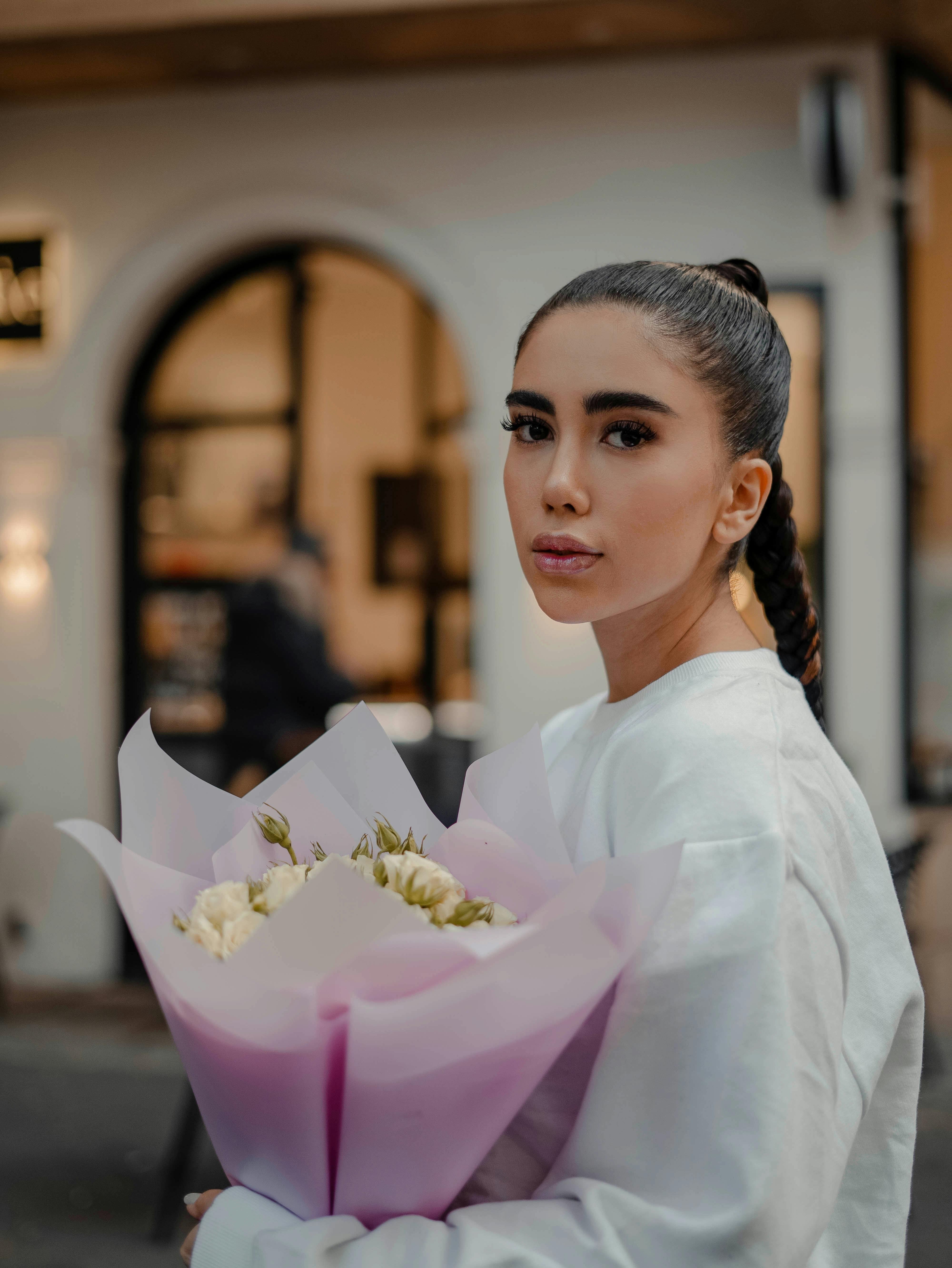 Stylish woman with braided hair holding a bouquet of flowers in an urban setting.