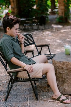 Person relaxing outdoors in garden seating with green beverage on stone table.