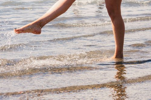 Free Close-up of legs in motion splashing water at a beach, evoking a playful summer vibe. Stock Photo