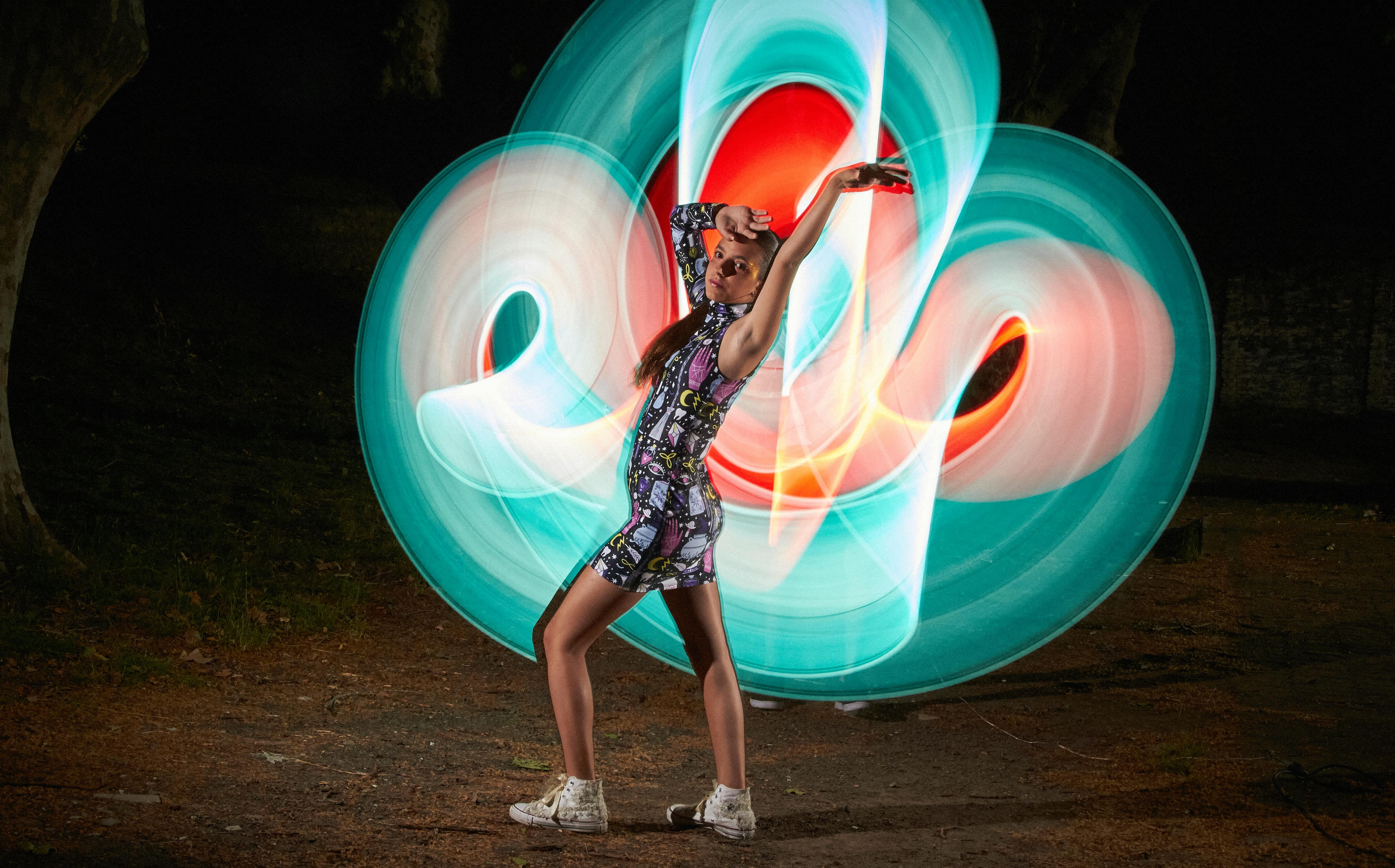 Artistic portrait of a woman dancing with vibrant light painting outdoors at night.