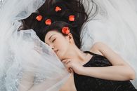 一位女子安详地躺在飘逸的布料和红色的玫瑰花瓣中，散发着优雅与宁静