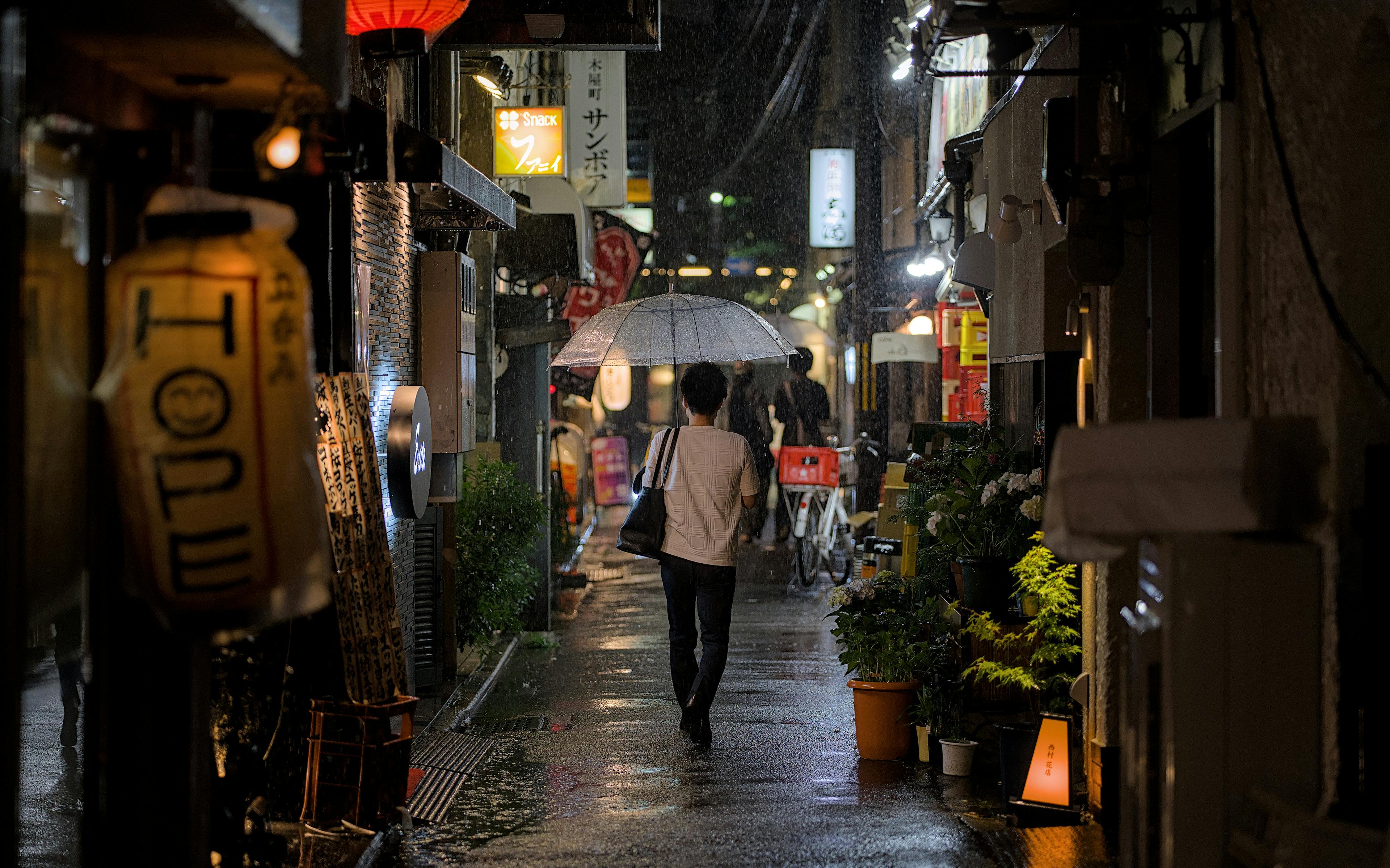 A person walks with an umbrella through a vibrant Kyoto alley at night.
