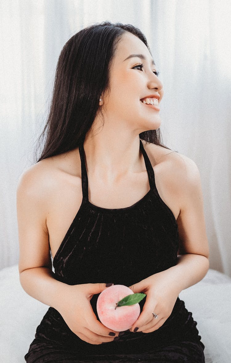 Cheerful Ethnic Woman In Velvet Dress Holding Peach