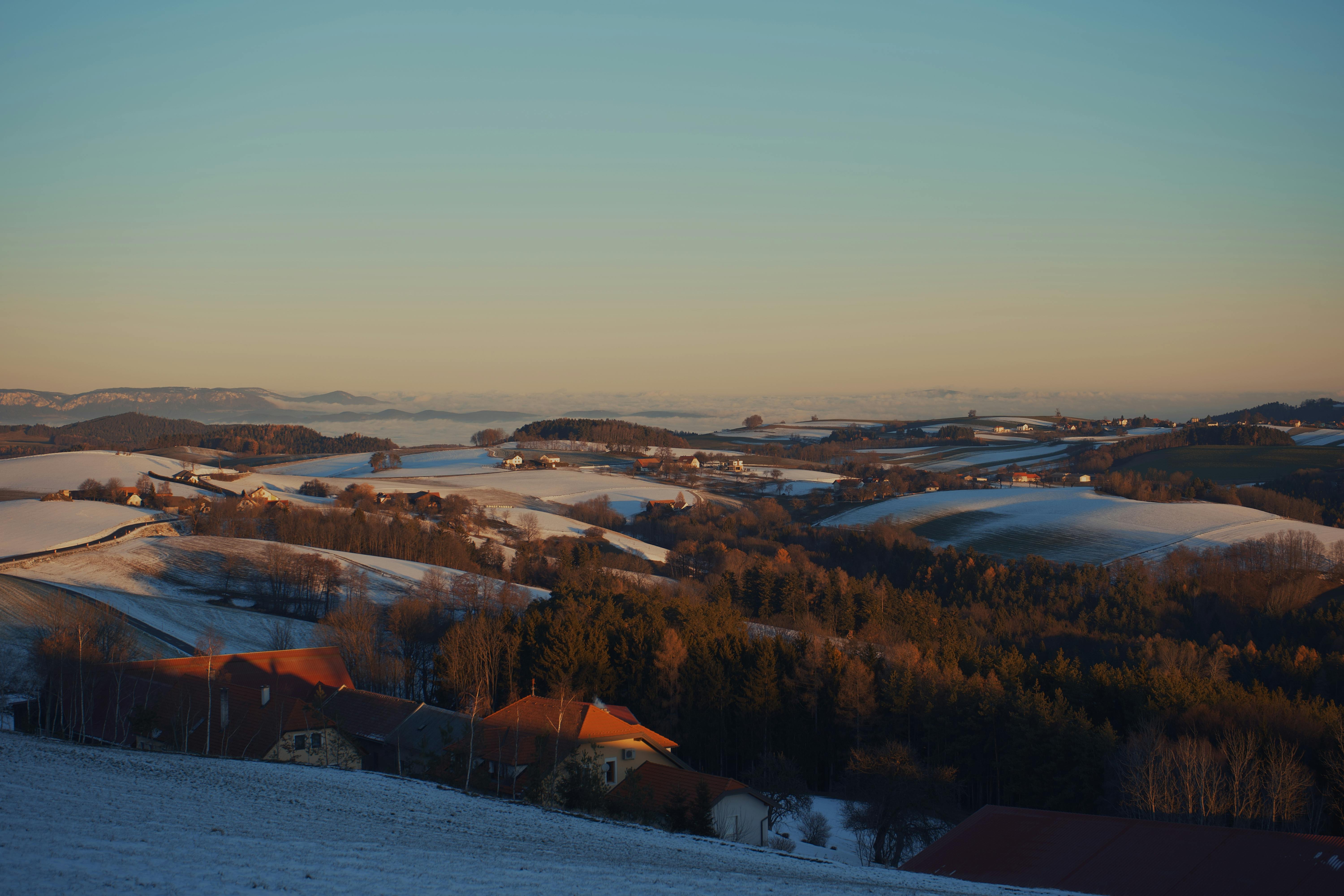 Breathtaking winter sunset over Austrian rolling hills with snow and greenery.