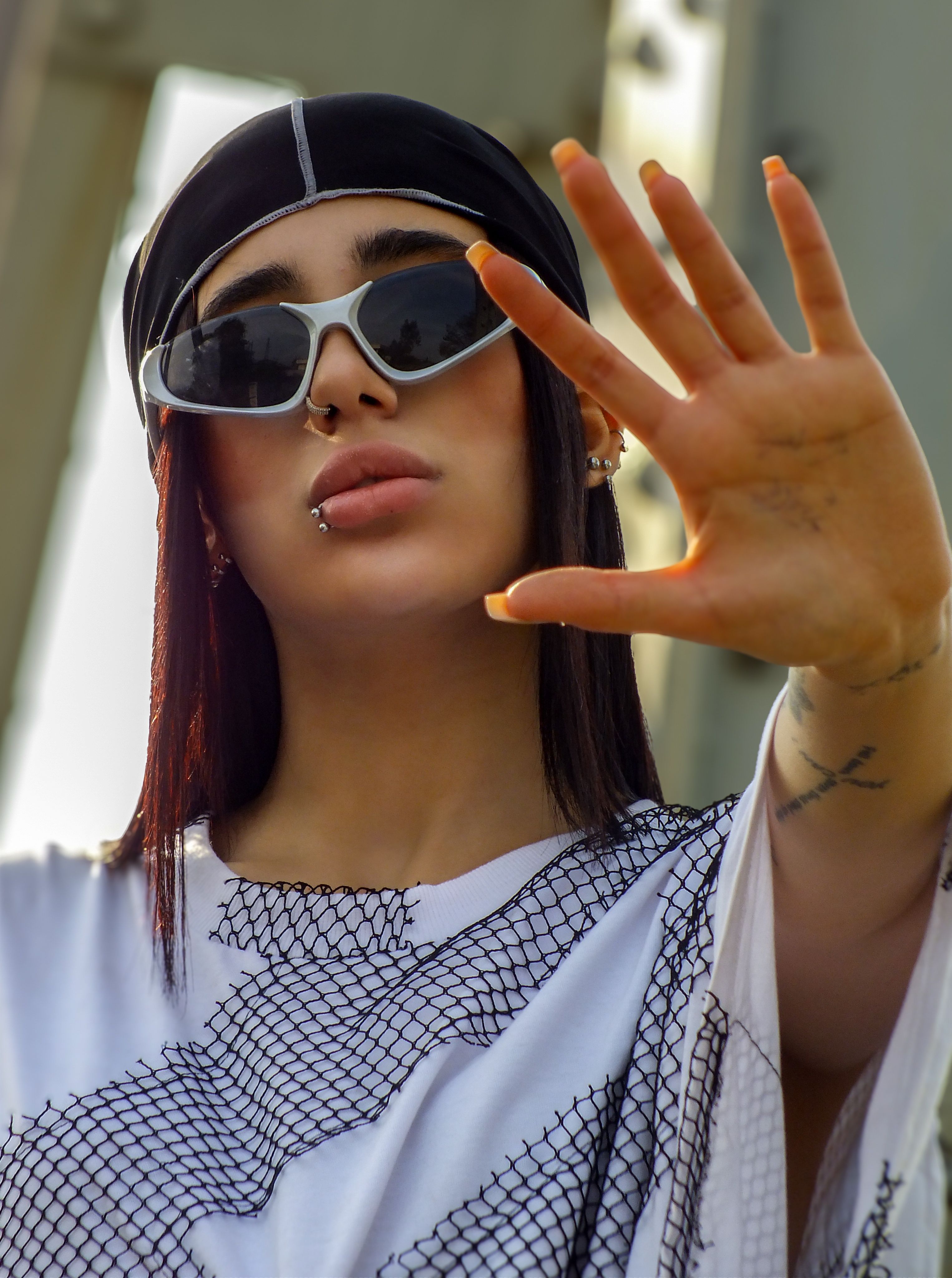 Fashionable young woman wearing sunglasses and a nose ring, making a hand gesture. Stylish and modern portrait.