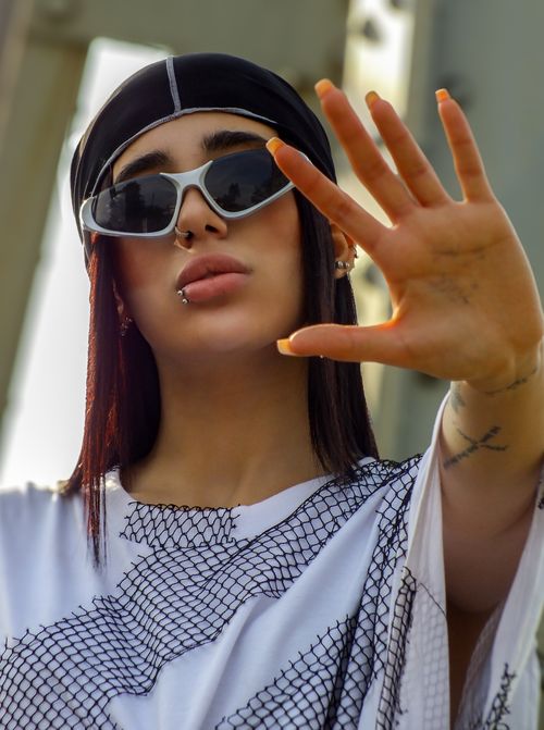 Free Fashionable young woman wearing sunglasses and a nose ring, making a hand gesture. Stylish and modern portrait. Stock Photo