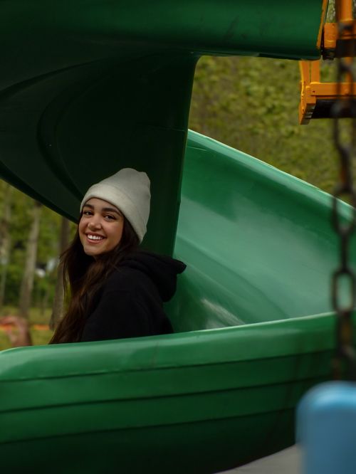 Free Asian woman in a park on a slide, wearing a beanie and smiling. Outdoor fun. Stock Photo