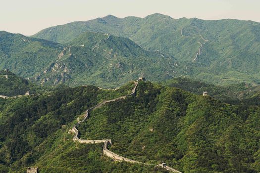 Aerial view of the Great Wall of China extending over lush, green hills in Beijing during spring.
