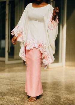 Stylish African woman in a pastel pink and white outfit with floral details.