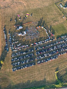 Aerial photo showing a vibrant outdoor music festival with a large crowd and parking area.