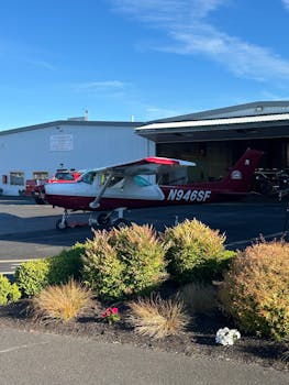 A red and white single-engine aircraft parked near a hangar under a clear blue sky.
