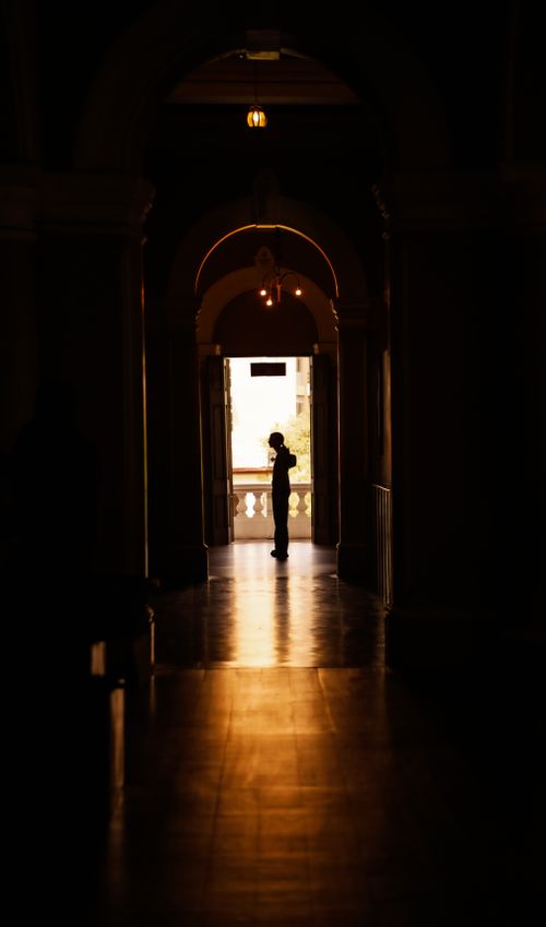 Free A lone silhouette stands in a historic hallway in Sri Lanka, creating dramatic contrast with light and shadows. Stock Photo