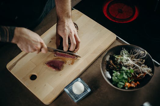A chef skillfully slices beef on a wooden board with fresh ingredients nearby.