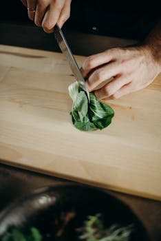 Close-up of a chef's hands slicing bok choy on a wooden board, ideal for culinary content.