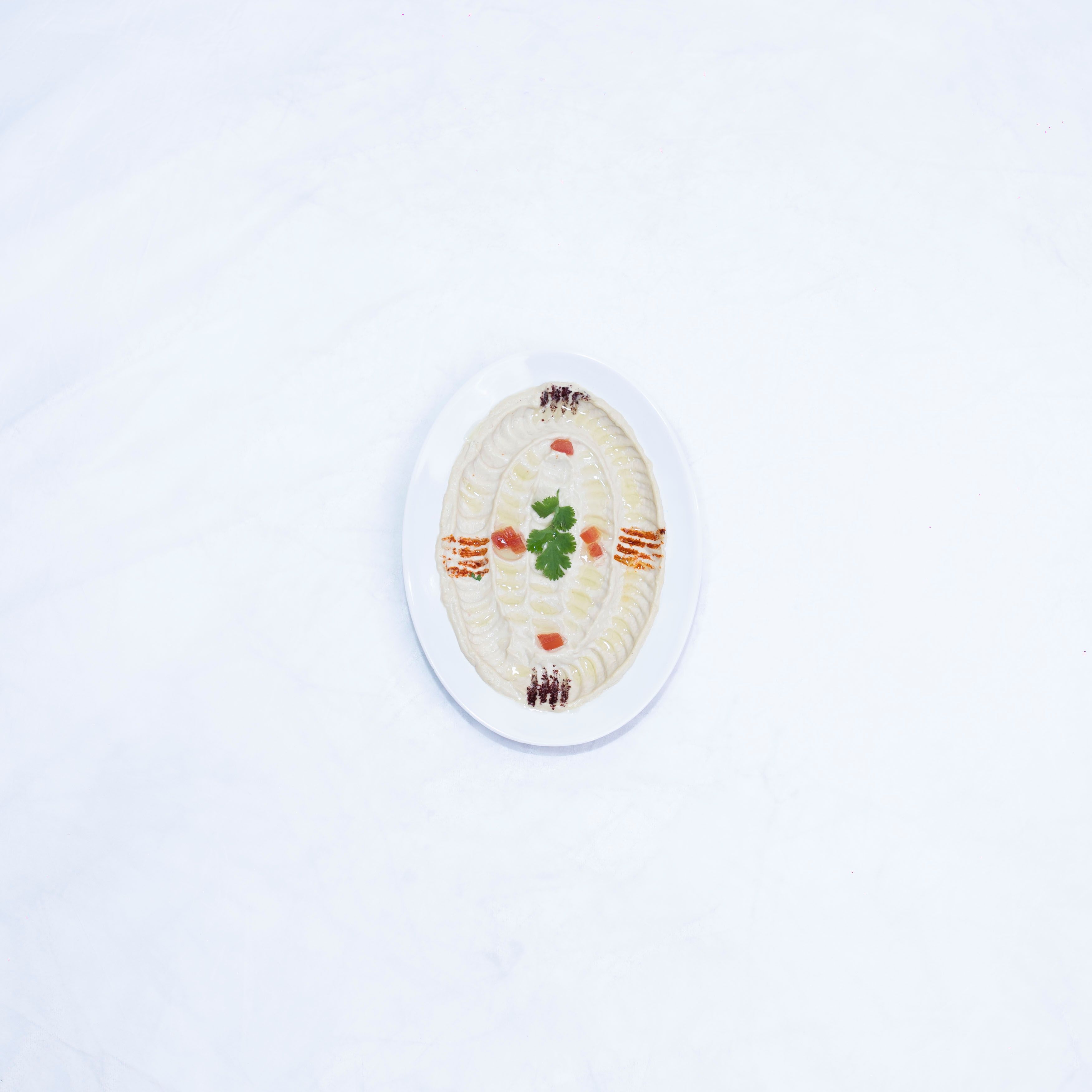 Overhead view of a garnished hummus dish on a clean white surface.