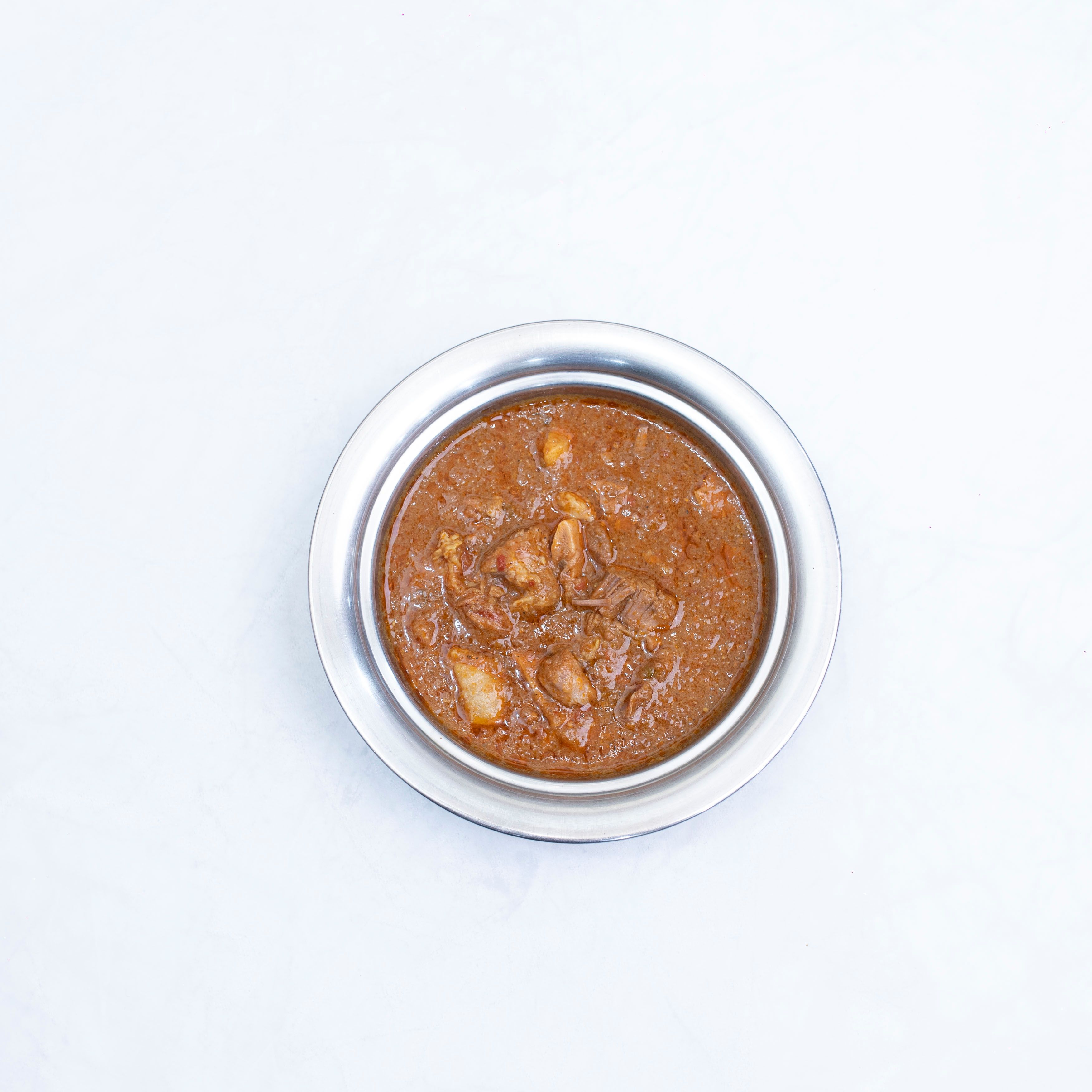 A top-down view of homemade chicken curry in a stainless steel bowl.