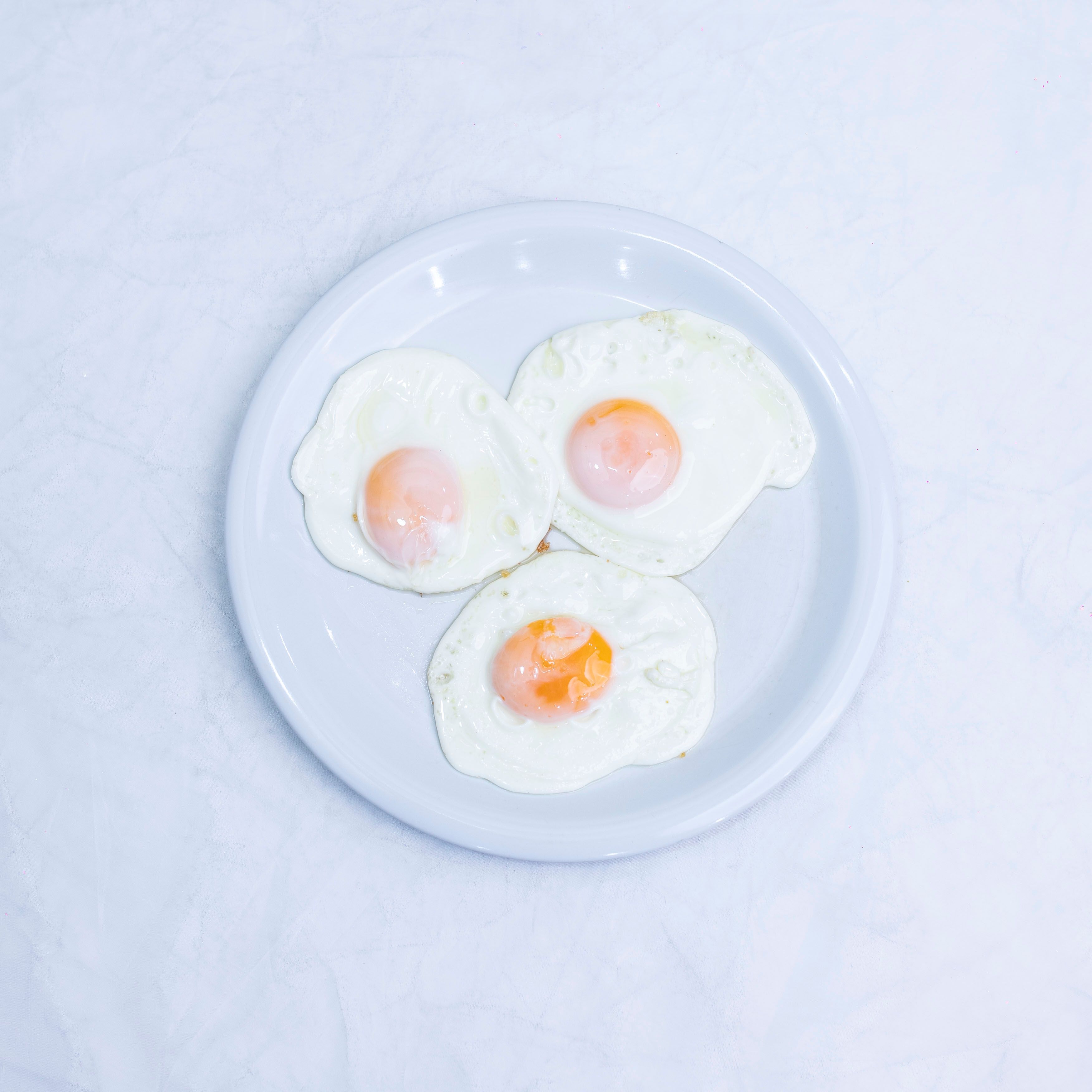 Three perfectly fried eggs on a white plate from a top-down perspective.