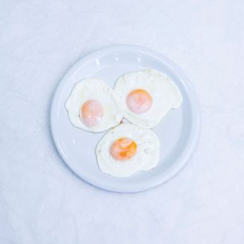 Three perfectly fried eggs on a white plate from a top-down perspective.