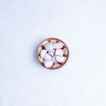 A flat lay of fresh onion pieces in a decorative bowl on a white marble surface.