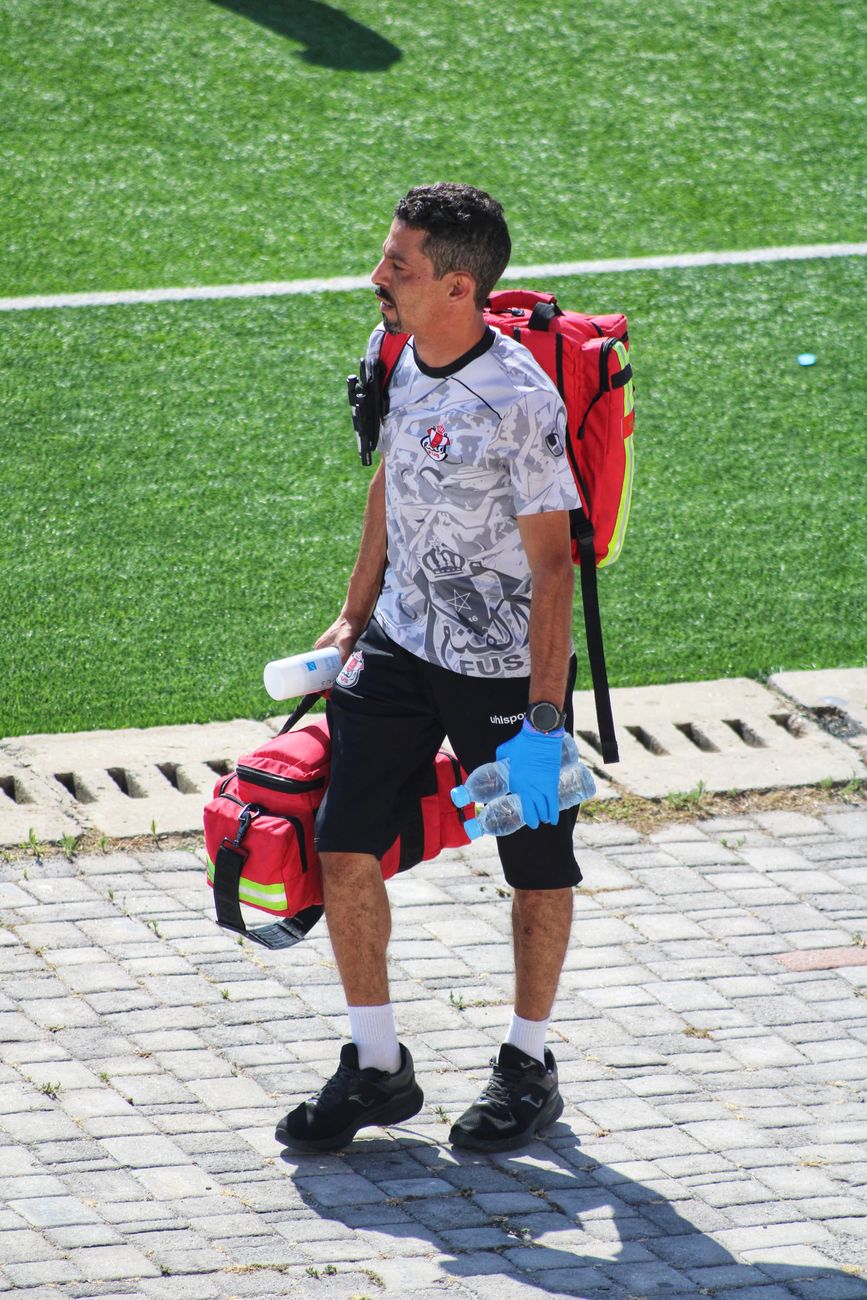 A football medic carrying emergency gear onto a community sports field before a match.