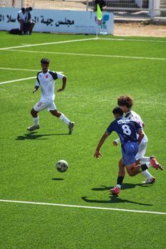 Teenagers playing an intense soccer match outdoors on a sunny day.