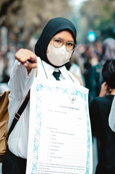 A woman wearing a mask and holding a sign participates in a public protest in Bandung, Indonesia. - Fotografer Sidoarjo