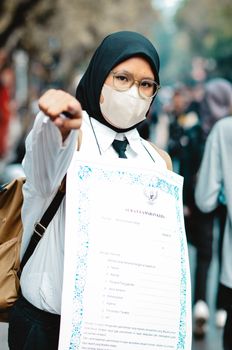 An adult cosplayer in a hijab and mask holds a certificate at a cosplay event in Bandung, Indonesia. - Fotografer Sidoarjo