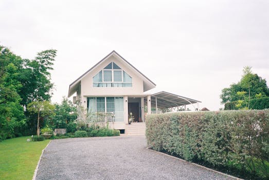 Charming suburban house with a green garden and driveway under a cloudy sky.