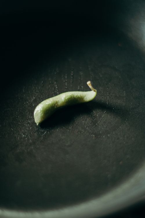 Free Close-up of a single edamame bean in a dark skillet, emphasizing simplicity and texture. Stock Photo