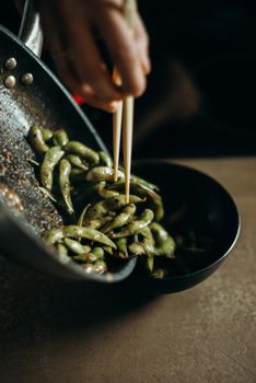 Close-up of cooked edamame being served with chopsticks, perfect for culinary themes.