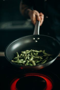 Close-up of edamame being cooked in a frying pan on an electric stove.