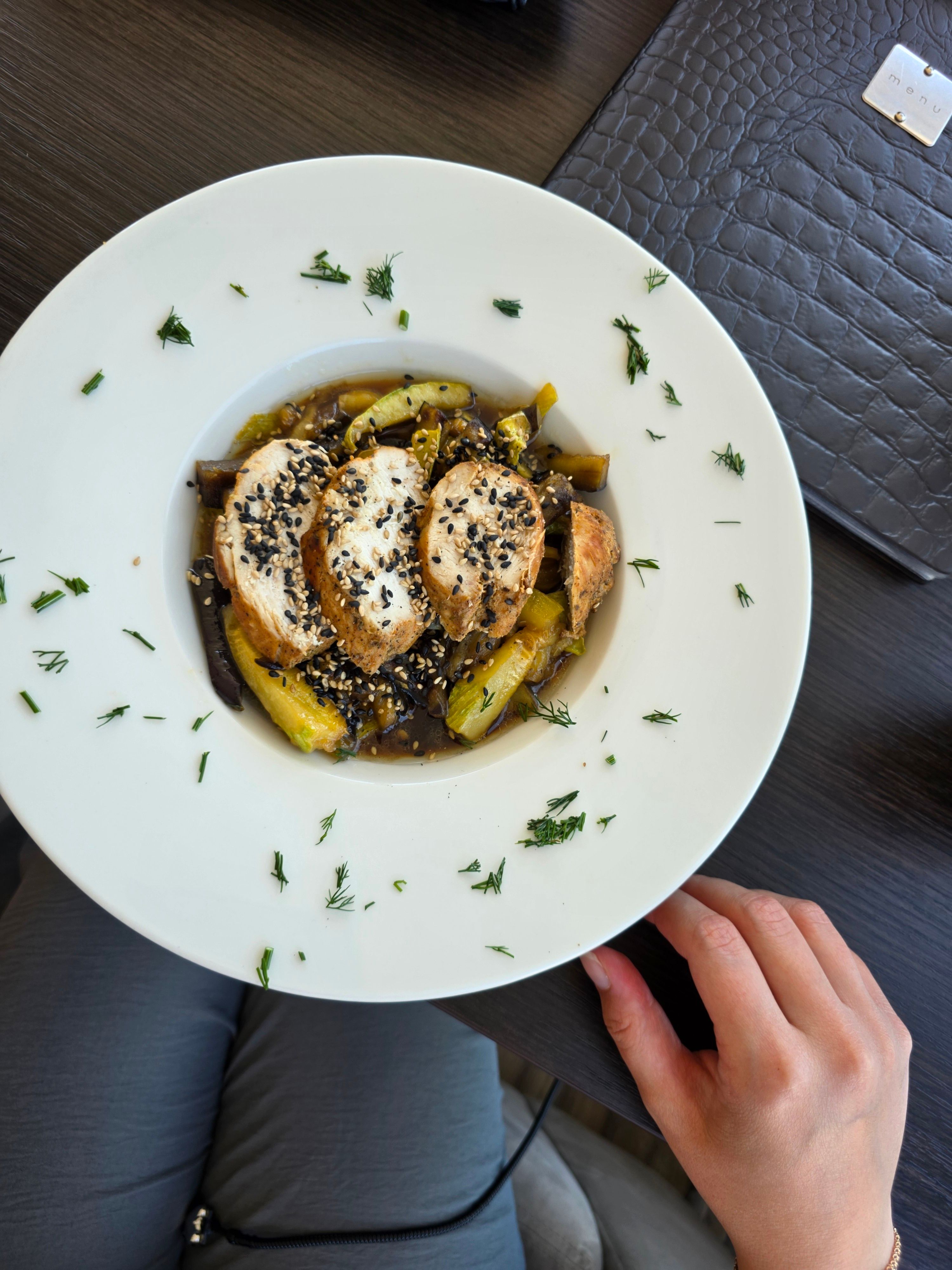 Grilled chicken served with sauteed zucchini and sesame seeds, garnished with herbs.