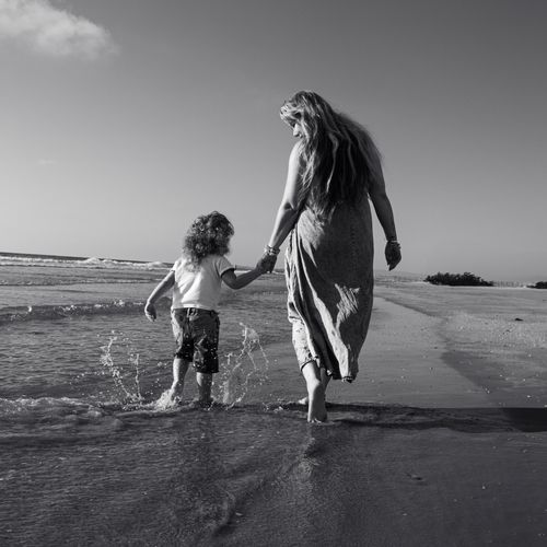 Free A serene black and white photo of a mother and child holding hands on a beach at sunset. Stock Photo