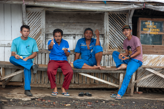Four men sit on a wooden bench outside an urban shop, enjoying a casual break.