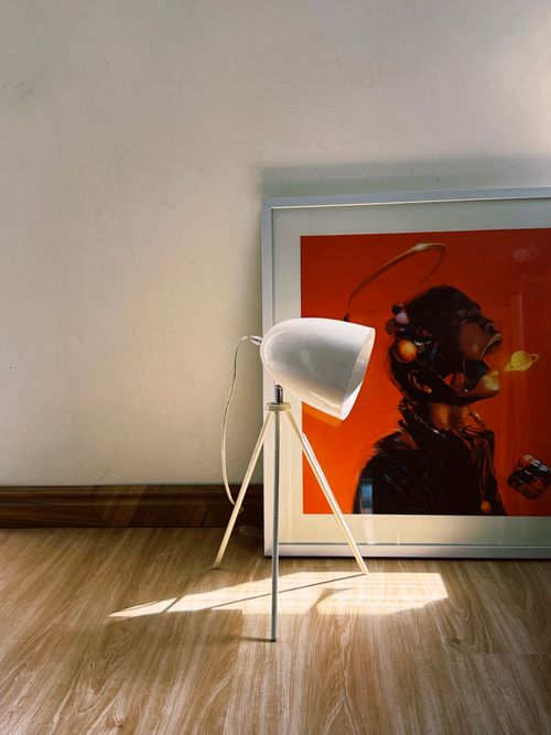 Free A stylish modern tripod lamp illuminates a vibrant artistic print in a cozy corner. Stock Photo