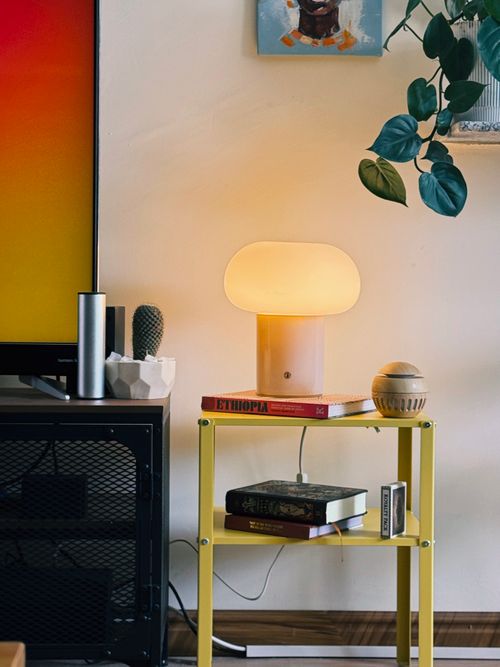 Free Modern living room with warm lamp, books, and decor on a yellow shelf. Stock Photo