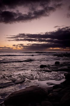 Moody sunrise at Sunshine Coast beach with clouds and rocky shore.